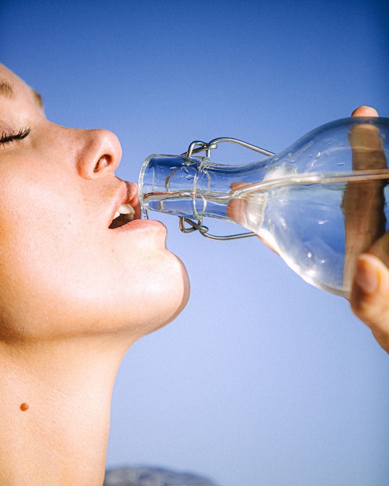 A woman drinking water outdoors under an open sky